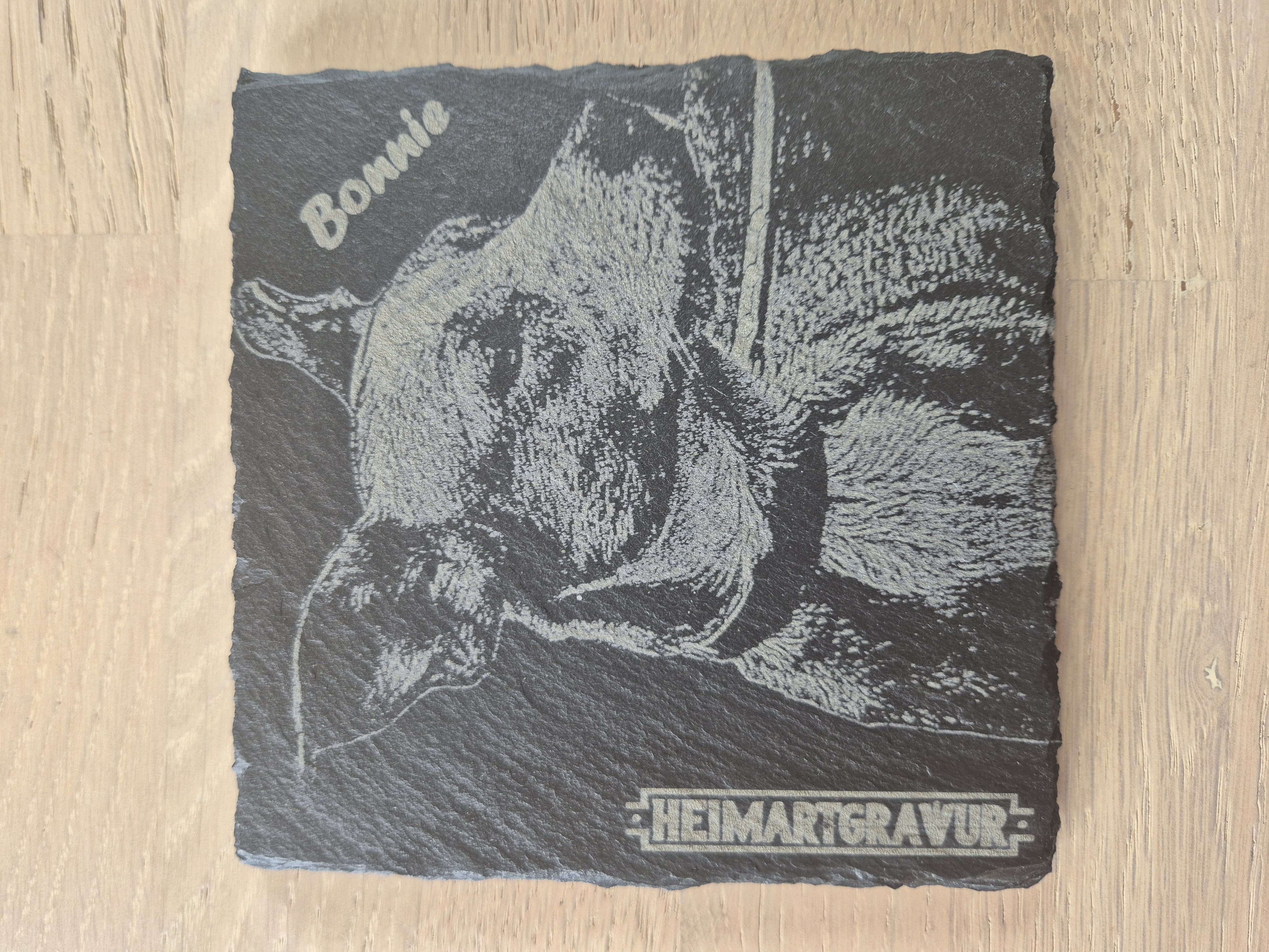 Fotogravur auf Schiefer im Format 13x13 cm inklusive dem Namen des Hundes und dem HeimArtGravur-Logo-Schriftzug.
